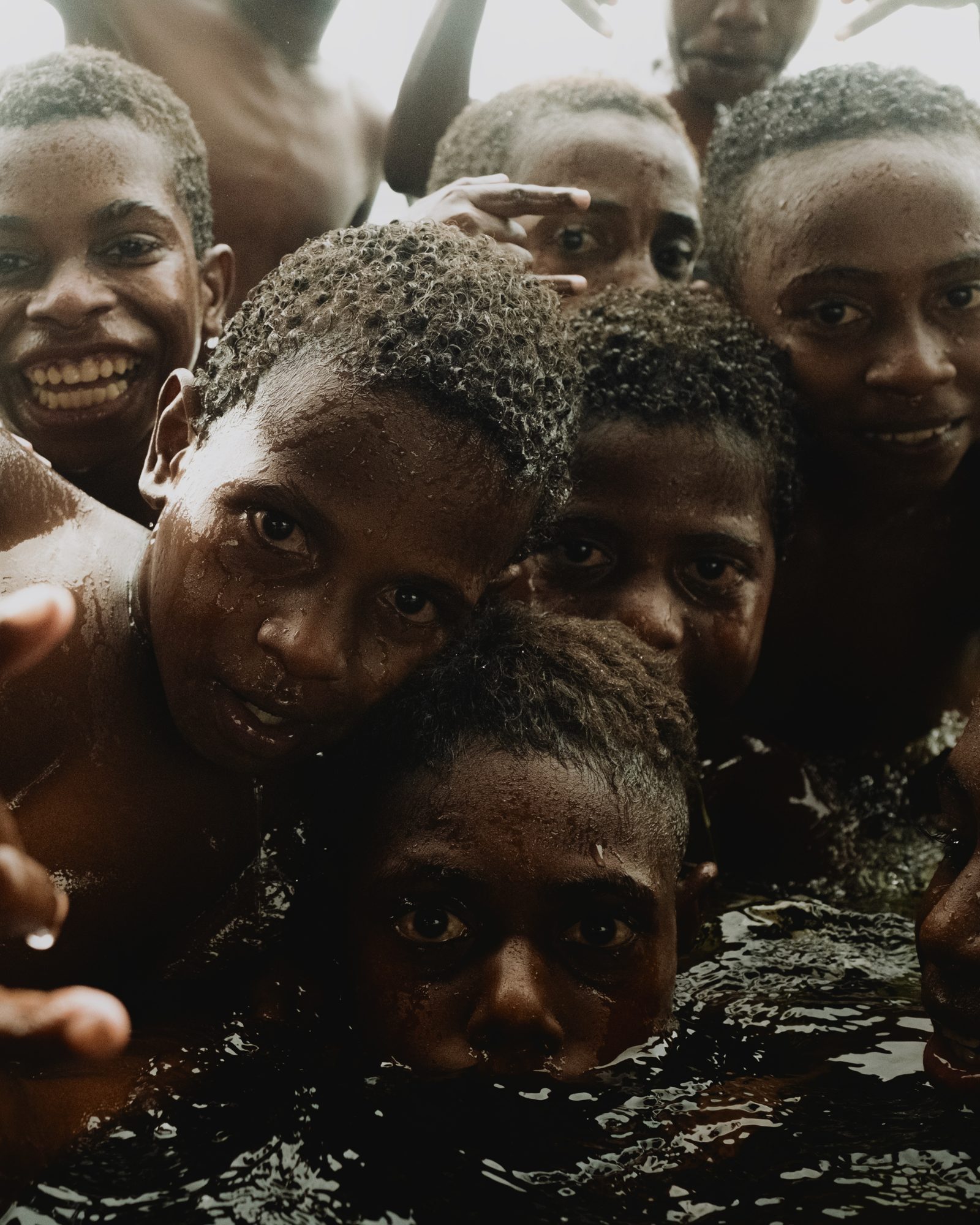 Children crowd together, smiling, in the water